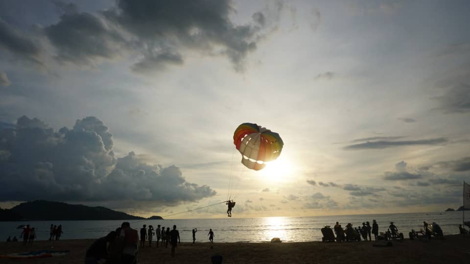 people on the beach for water sports at sunset. Parasail in the air